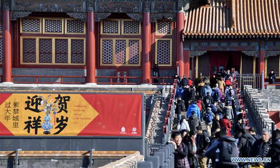 Tourists walk past a poster celebrating the Spring Festival in the Palace Museum, also known as the Forbidden City, in Beijing。(Xinhua/Li Xin)